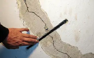 A wall with a large crack is being inspected by a professional in Stockton, CA